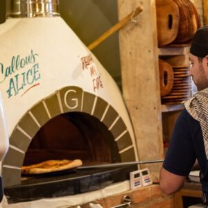 Chef weaing a red cap cooking food in pizza oven